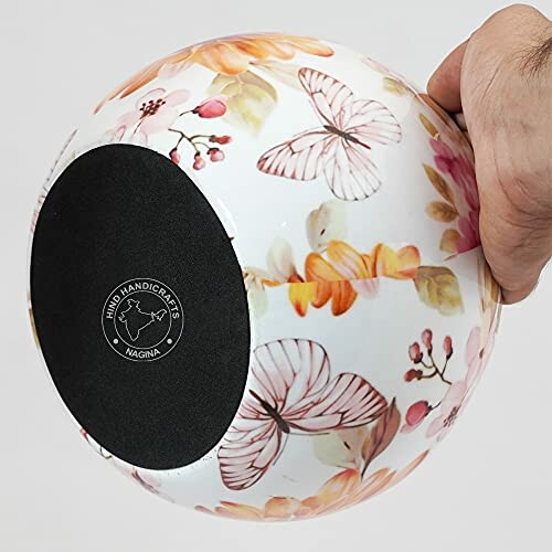 Hand holding a decorative globe with floral and butterfly design.